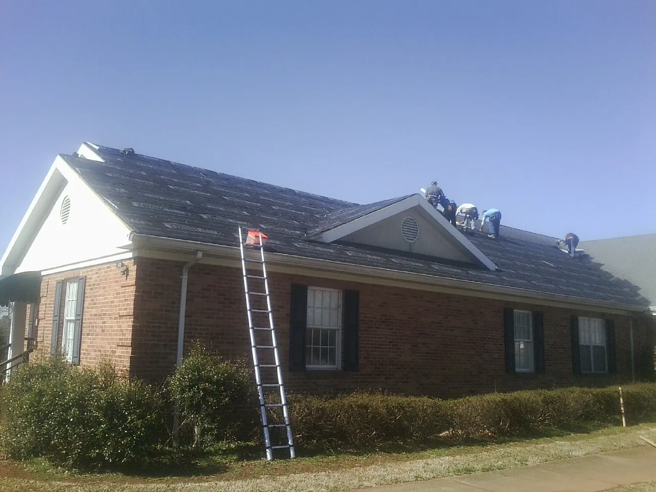 Crew tearing shingles off a brick ranch roof with a ladder set — Emergency Roof Repair work by our crew in Lowry