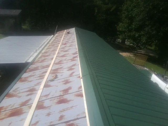Old rusted panels beside newly installed green metal roofing — Wind Damage Roof Repair by Roofing Brothers in Lowry