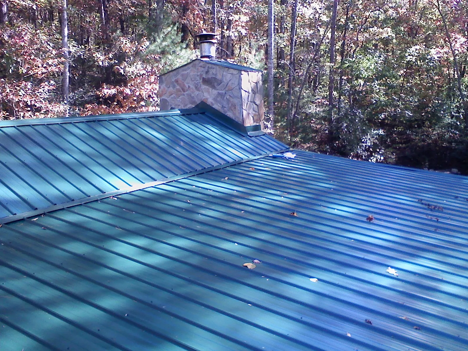 New green metal roof and stone chimney surrounded by autumn woods in Lowry