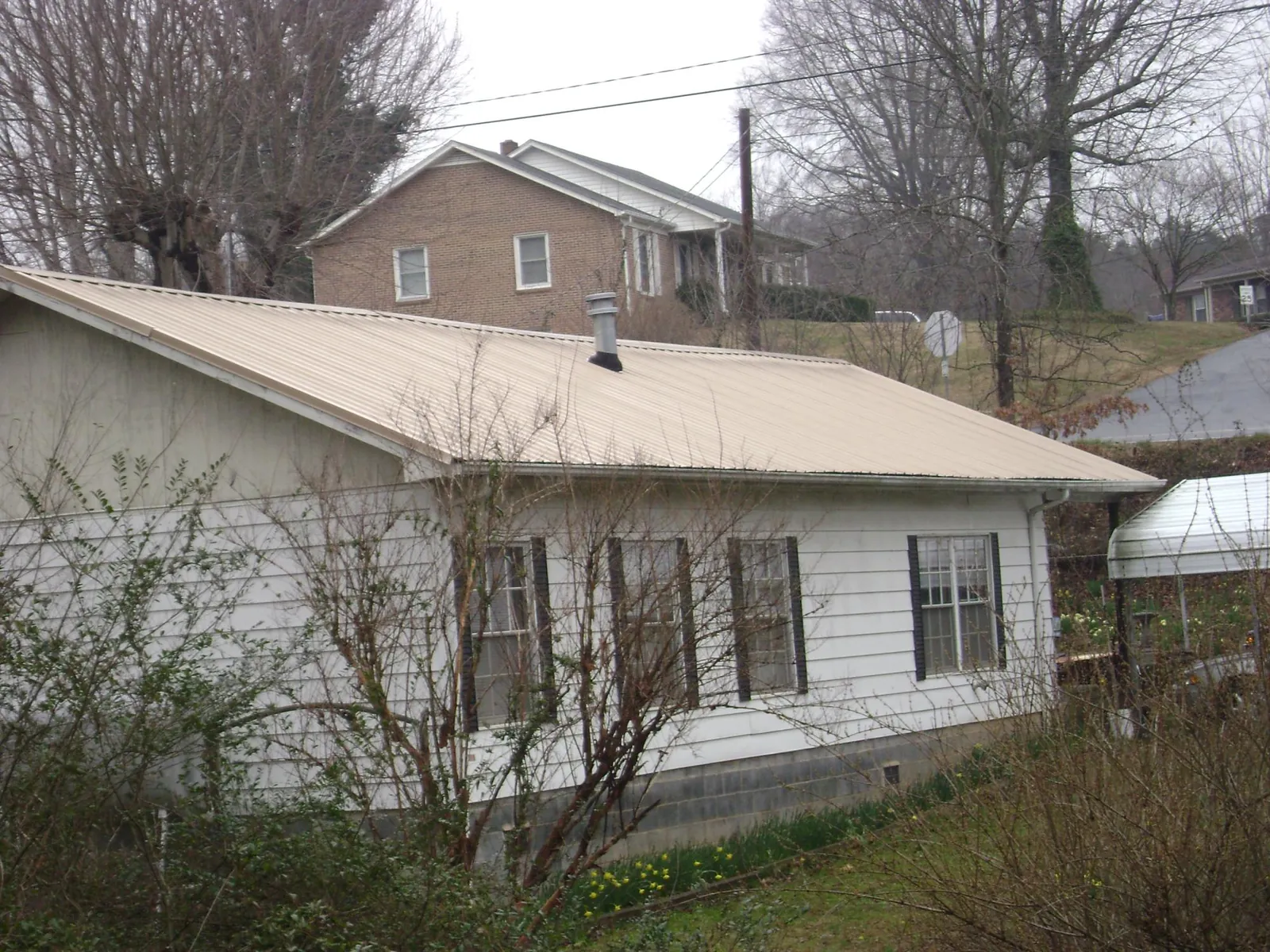Tan metal roof on a white sided house set into a hillside — Commercial Roofing by Roofing Brothers in Lowry