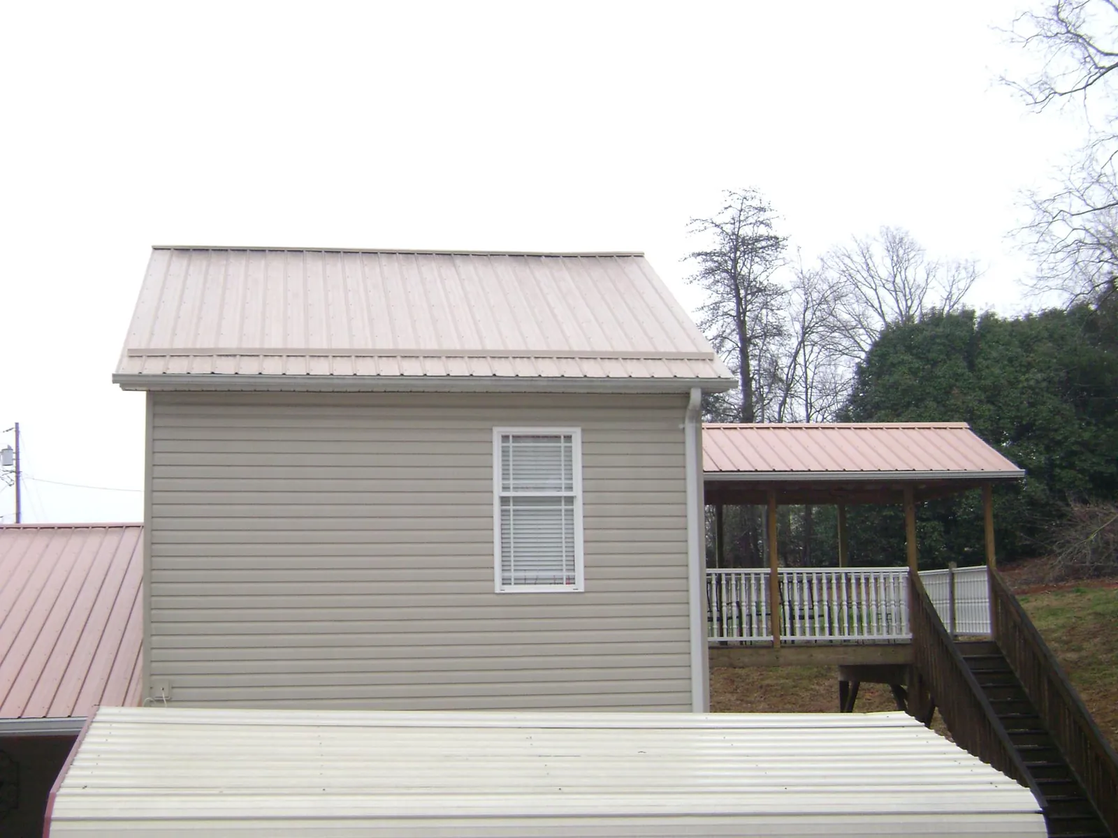 Tan metal roofs on a two story addition and attached porch, from a Roof Replacement job in Lowry